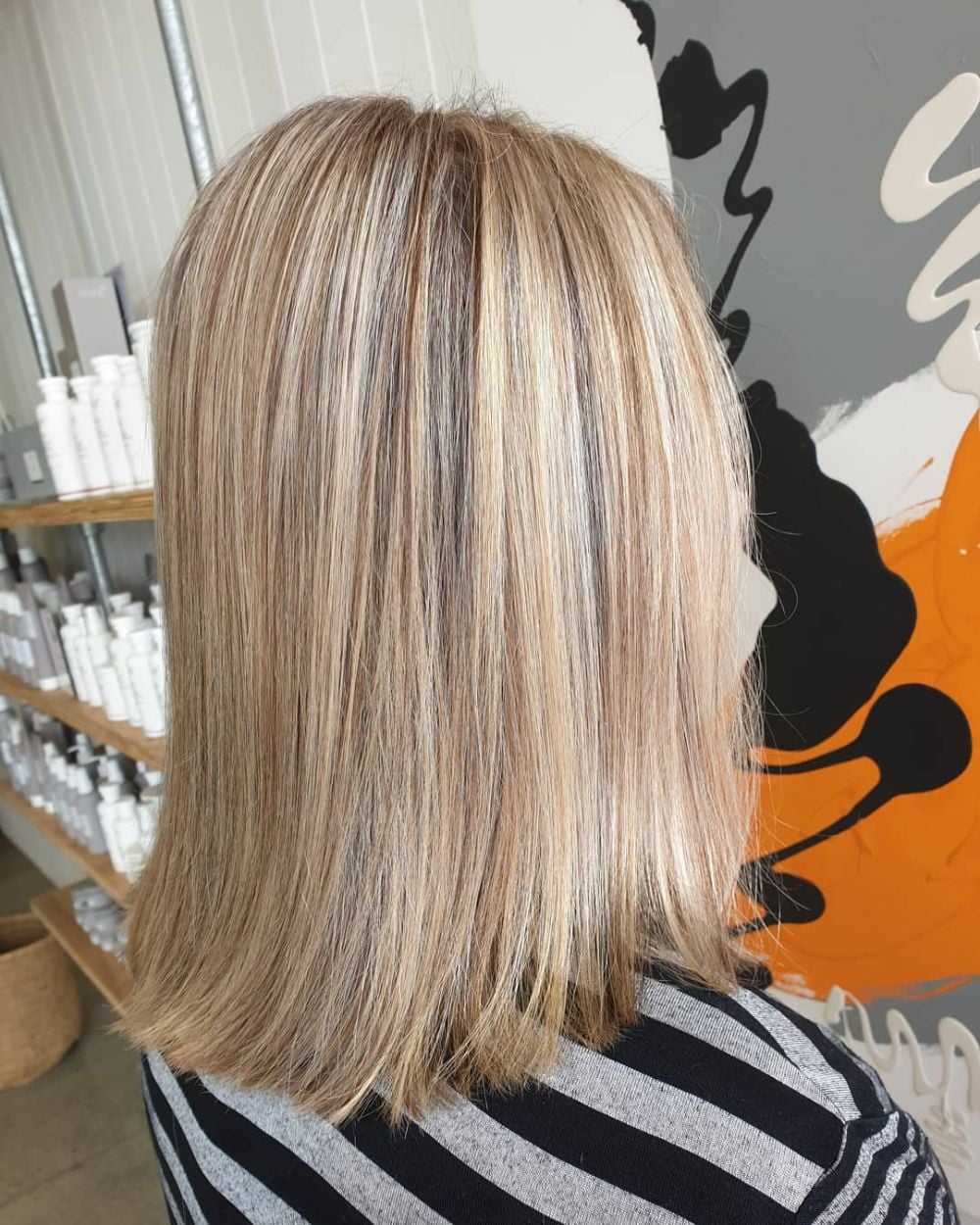 Blonde highlights and lowlights on a straight bob, the salon's shelves behind.